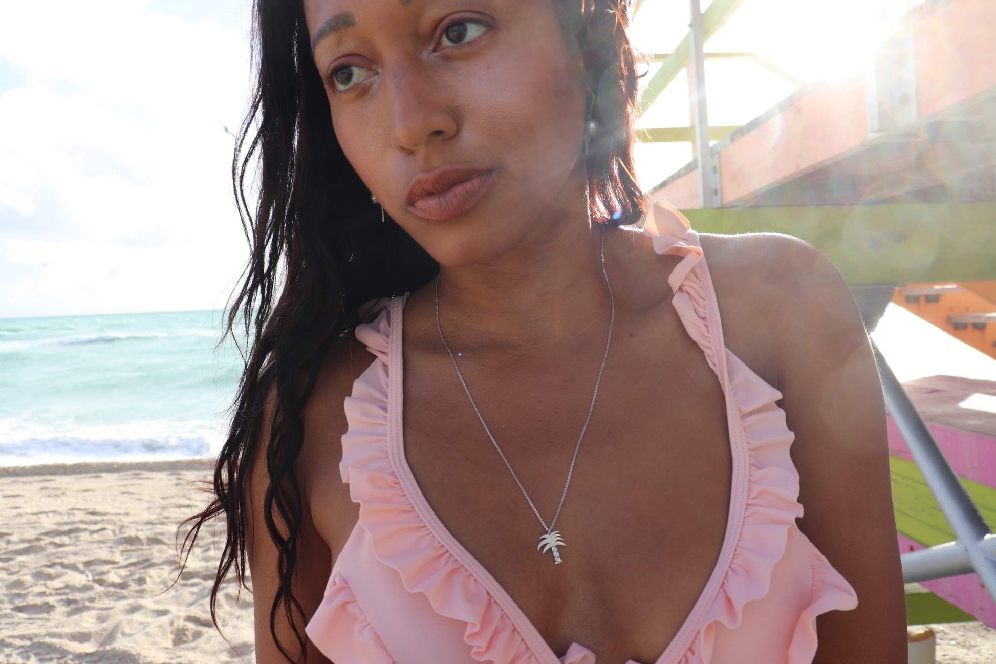 woman on beach in pink bikini wearing the palm tree pendant from the wandering jewel