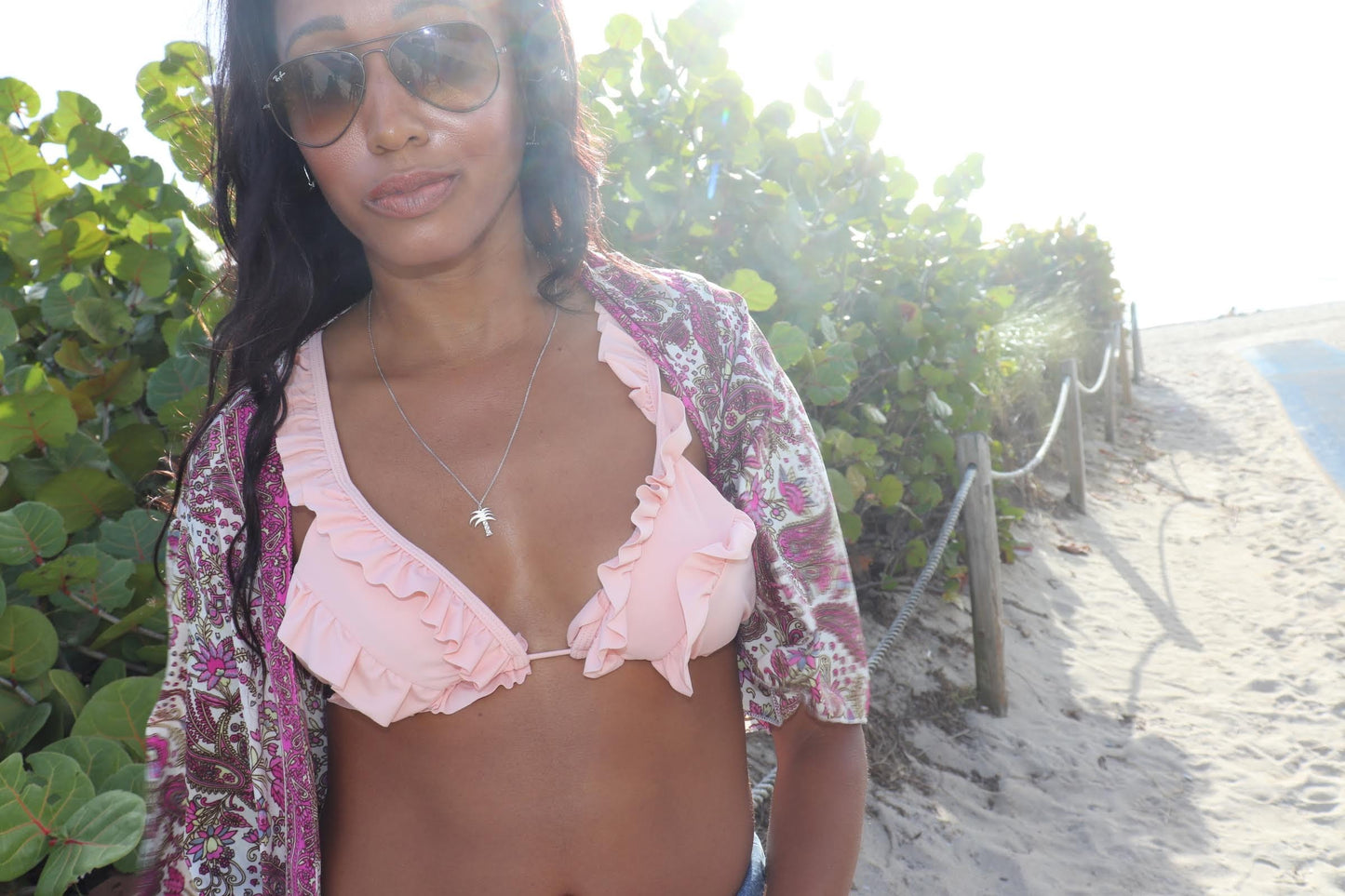 woman on beach in pink bikini and matching paisley jacket in sunglasses wearing the palm tree pendant from the wandering jewel