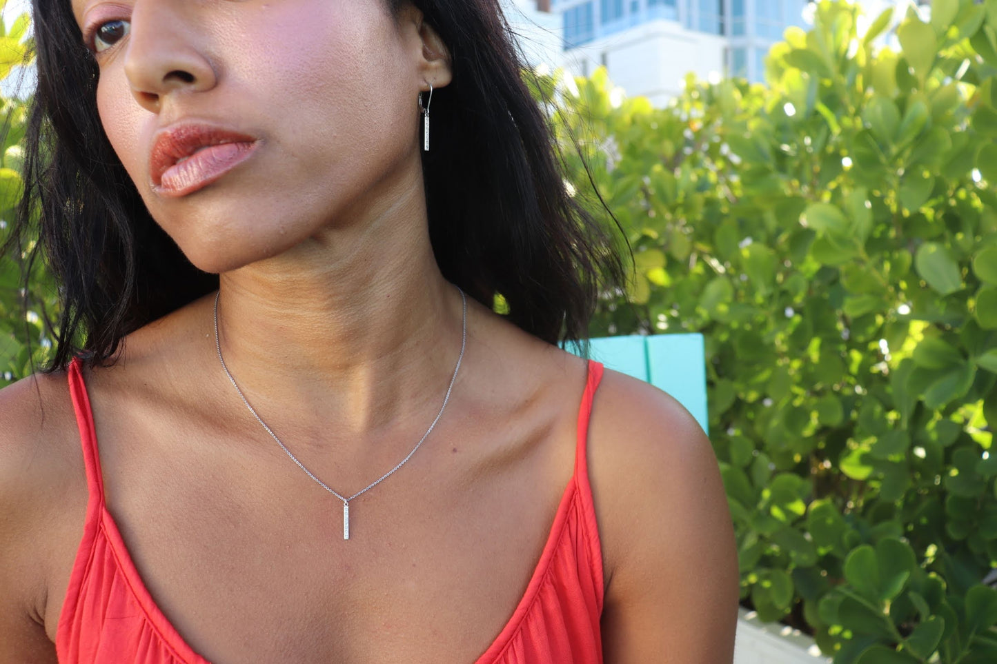 woman in orange top wearing  the 7 diamond pillar necklace and matching earrings from  the wandering jewel