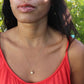 black woman with long brown hair and an orange shirt sitting in a garden and wearing the golden South sea pearl necklace from the wandering jewel
