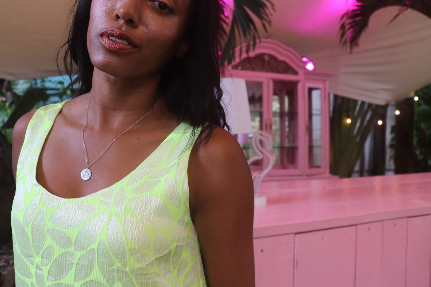 black woman in neon yellow dress in pink room wearing the 7 diamond coin necklace from the wandering jewel