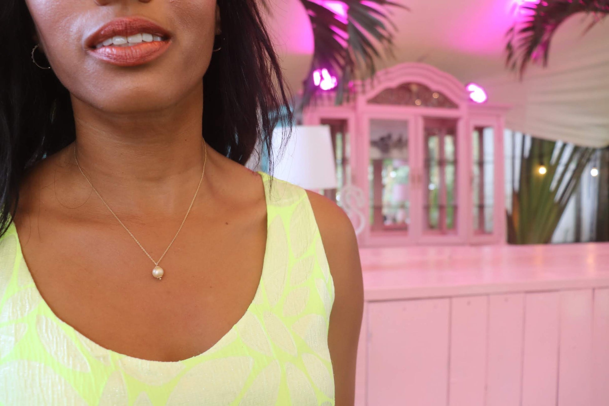 black woman in a neon yellow dress standing in a pink room  and wearing a the golden South sea pearl pendant necklace from the wandering jewel