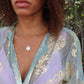 woman i a purple bikini and a matching aqua robe wearing the yahweh coin necklace fro the wandering jewel