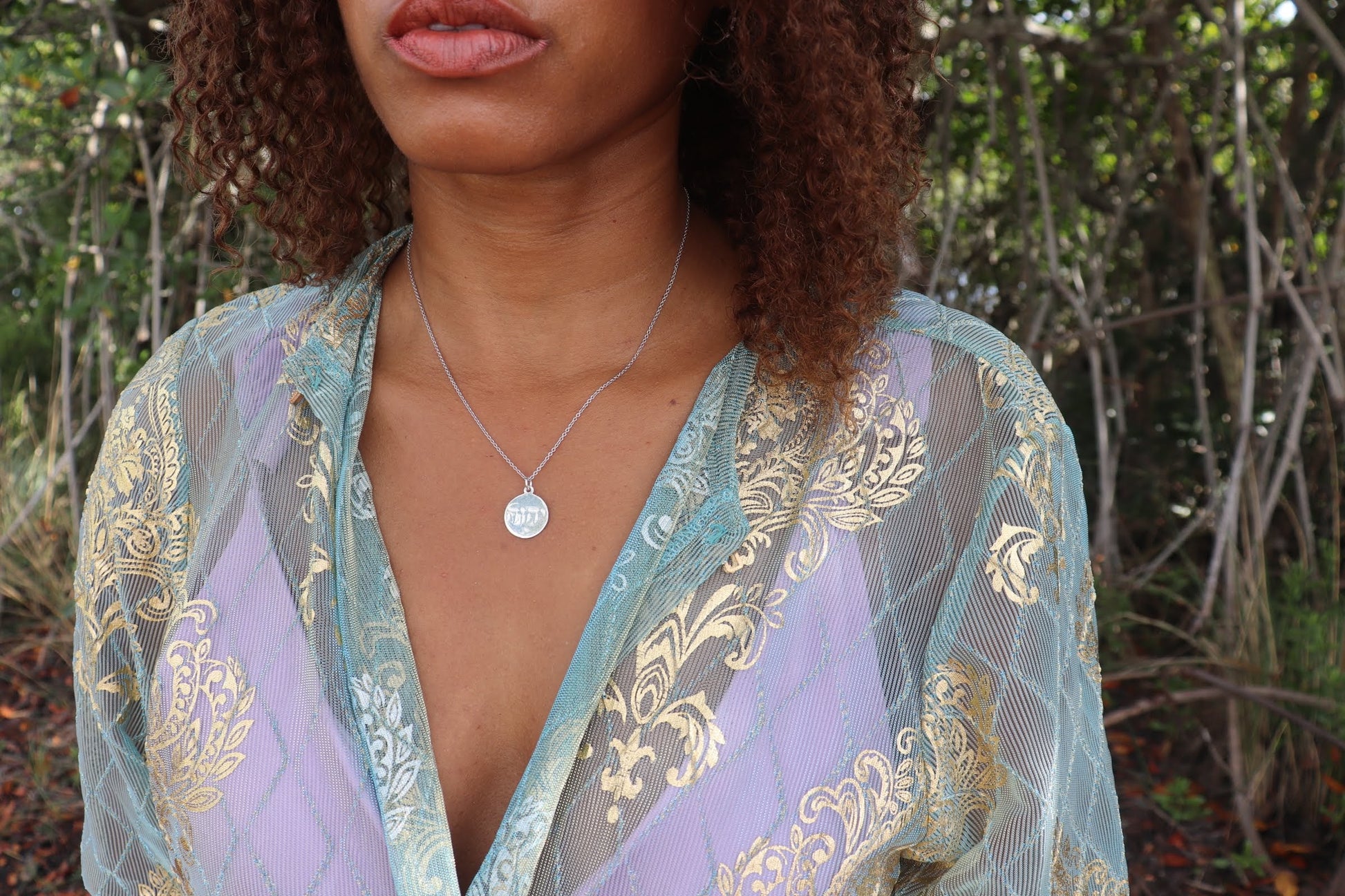 woman i a purple bikini and a matching aqua robe wearing the yahweh coin necklace fro the wandering jewel