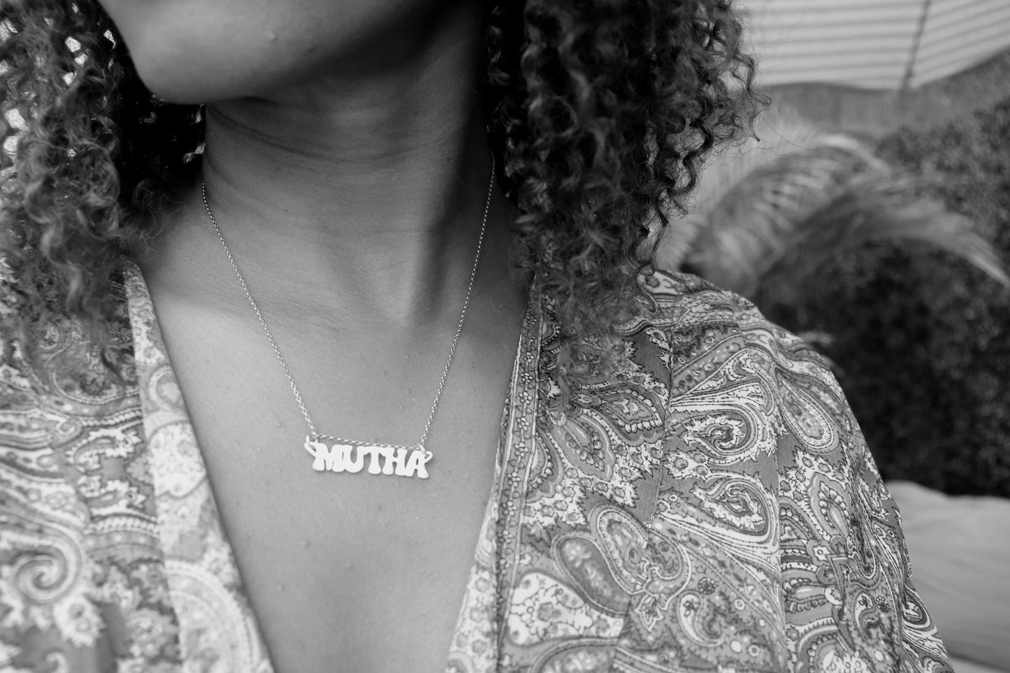 woman with curly hair wearing a paisley top and the  groovy mutha necklace from the wandering jewel