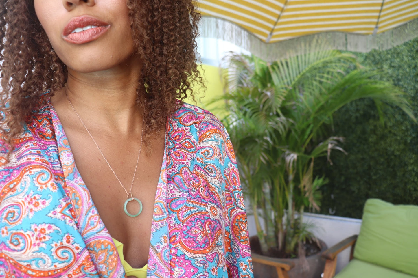 black woman in yellow bikini and paisley cover up wearing the 18K Solid Rose Gold green jade ring on rose gold necklace from the wandering jewel