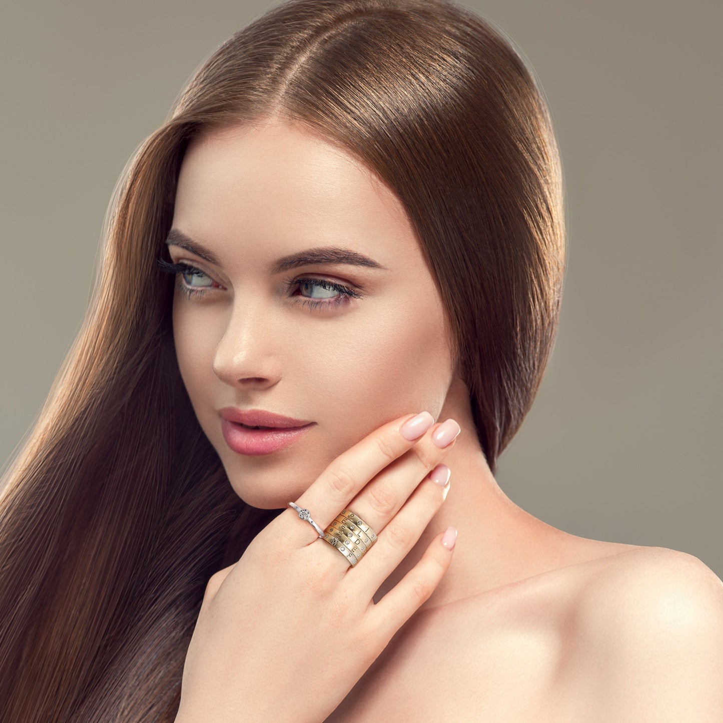 brunette woman looking over her right shoulder and wearing multiple gold  disengagement rings that have 7 gray diamonds from the wandering jewel