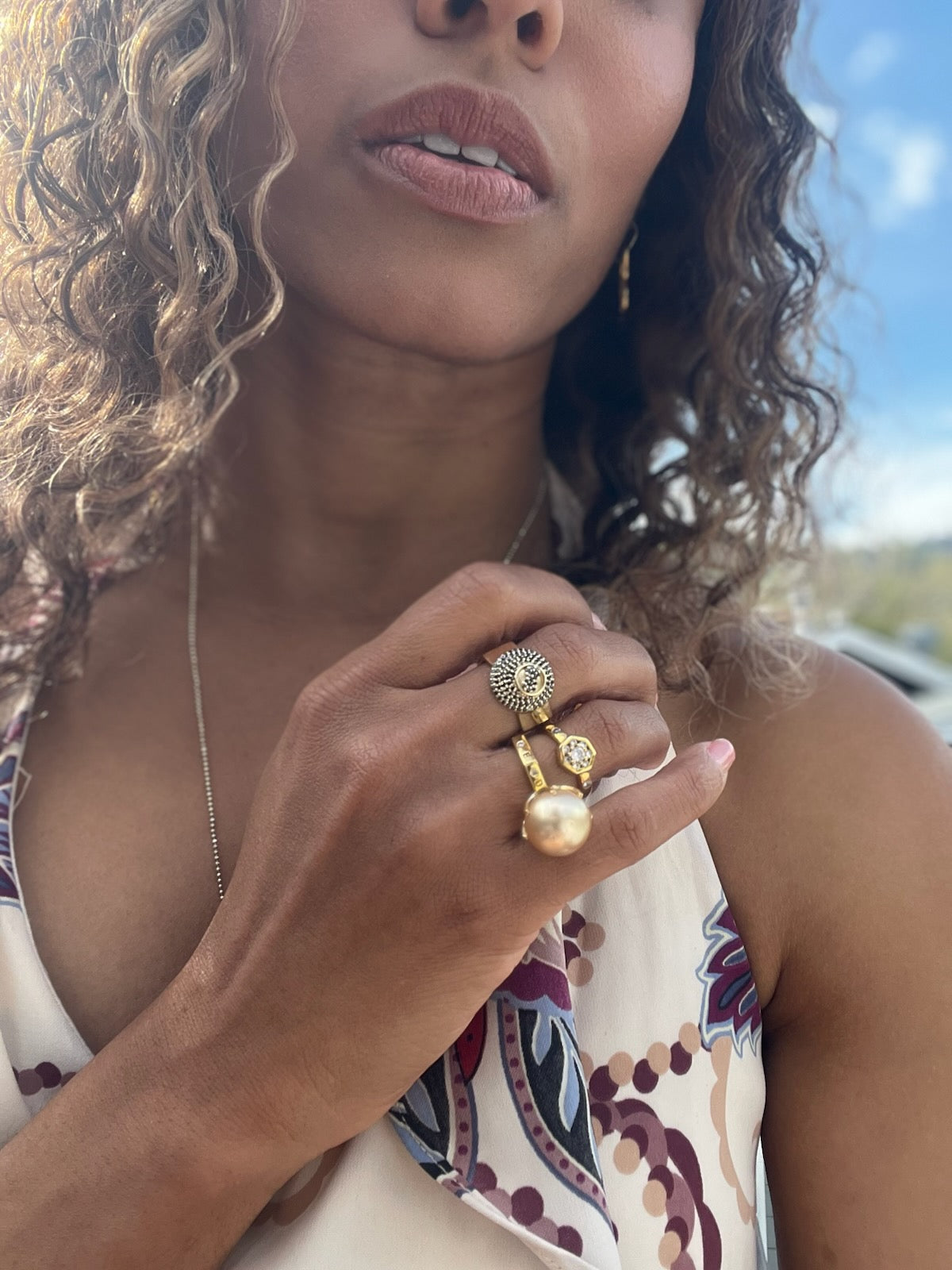 Black woman in floral dress outside on beach wearing the infinity Gold 8 sided octagon ring with an eight ball inscribed in black diamonds from the wandering jewel