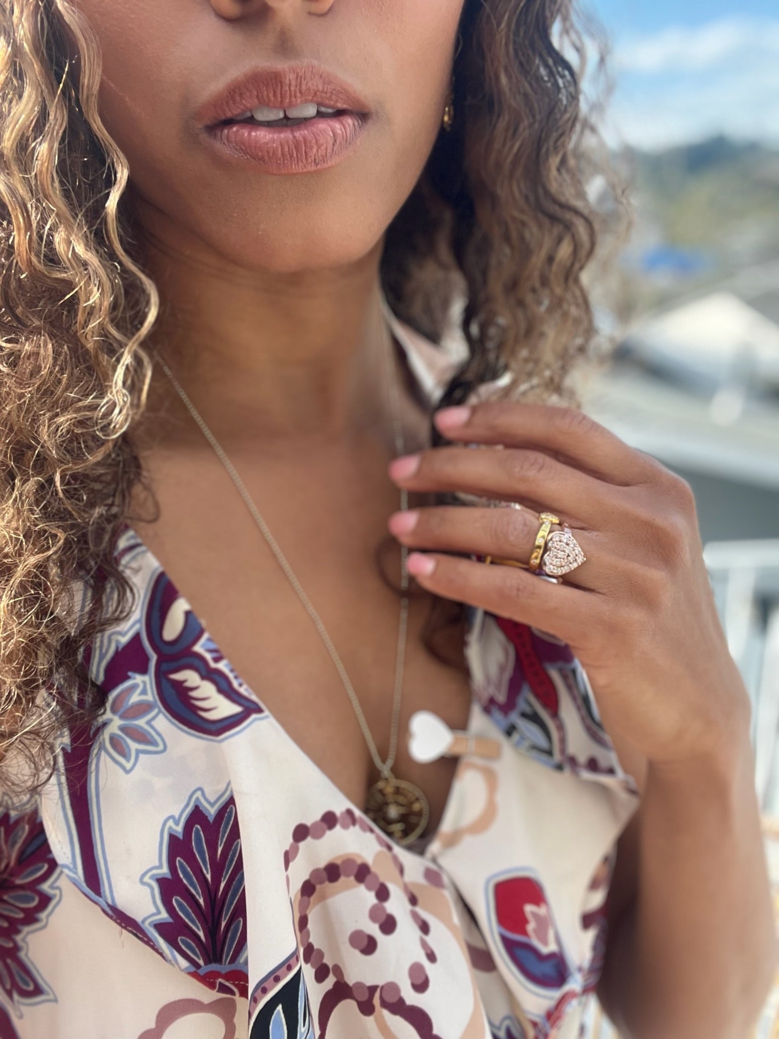 Black woman in floral dress on beach showing off her large puff heart diamond ring from the wandering jewel