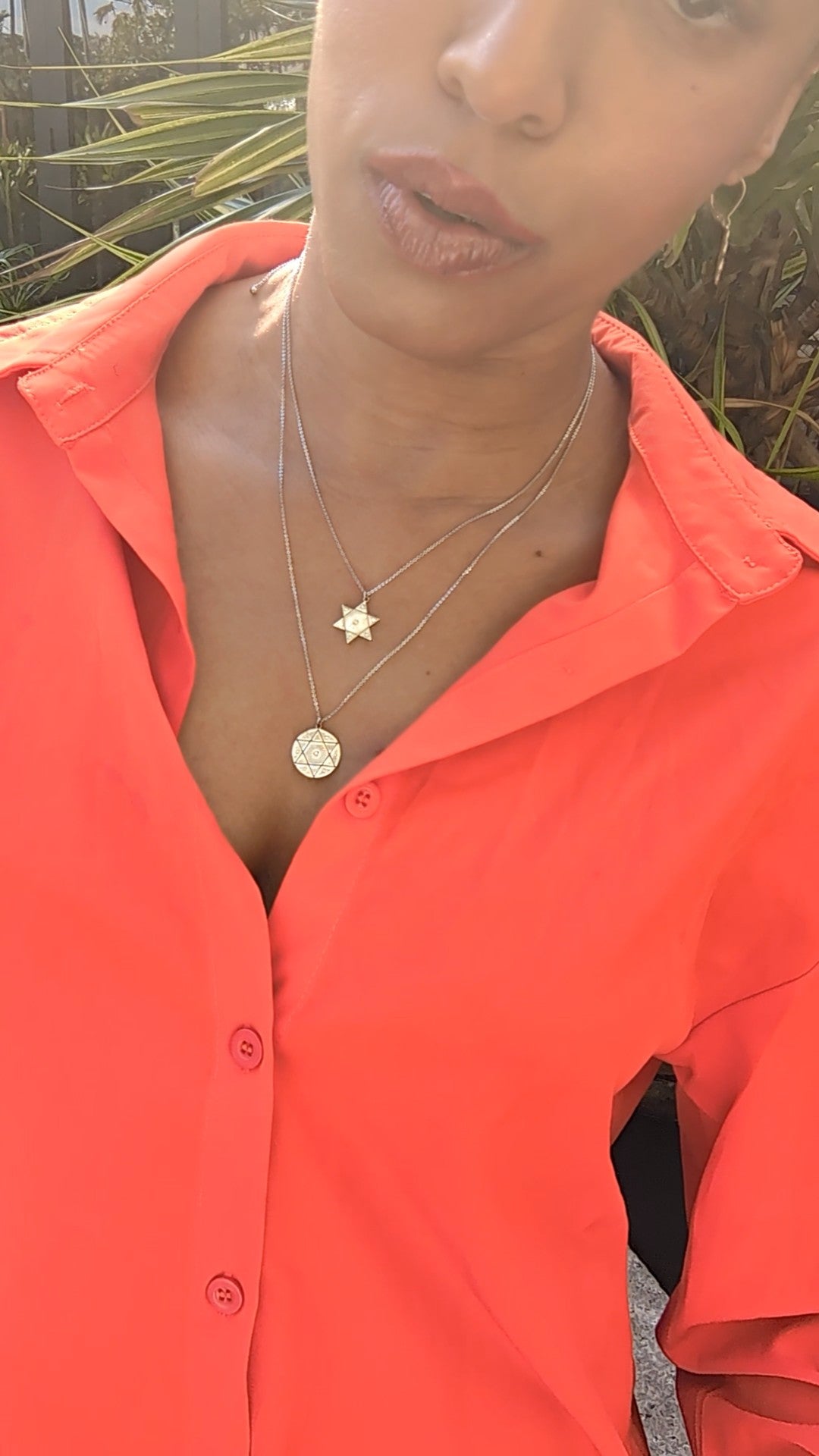 woman in an orange button up blouse wearing the wandering jewel's 7 diamond star of david pendant and coin necklaces from the wandering jewel