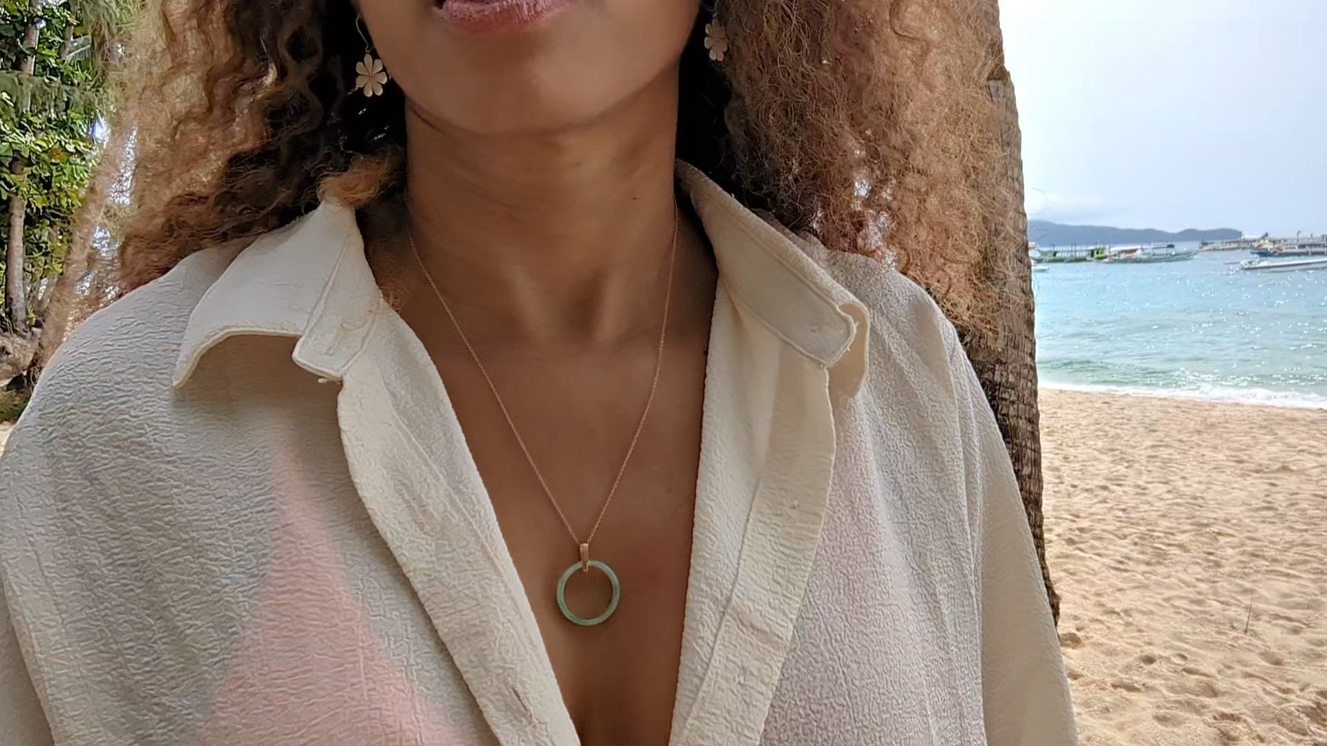 black woman in orange bikini and oversized white blouse on beach wearing the 18K Solid Rose Gold green jade ring on rose gold necklace from the wandering jewel