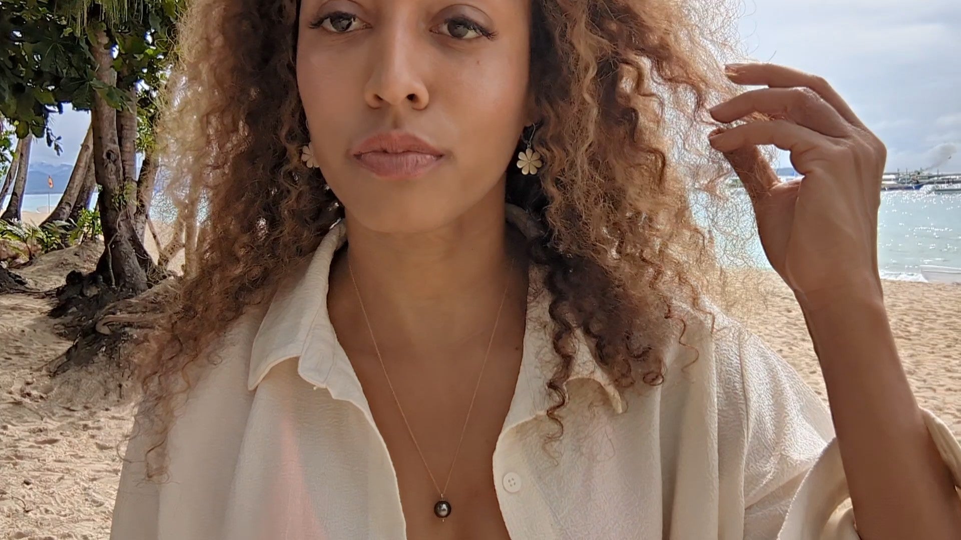 black woman with curly hair on beach in bikini with oversized white blouse wearing the black South sea pearl pendant from the wandering jewel