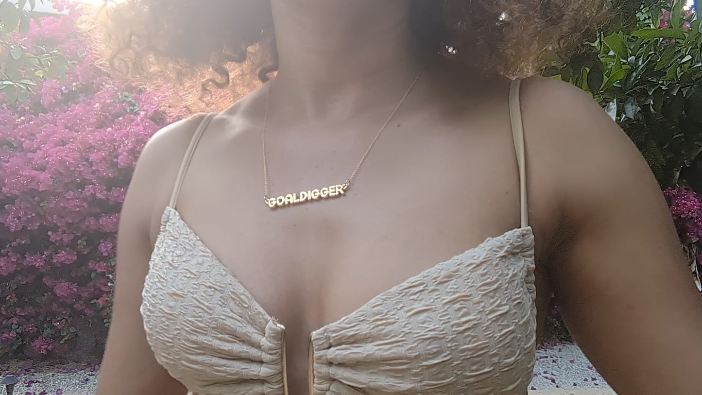 woman in tan bikini top wearing the gold goal digger necklace from the wandering jewel
