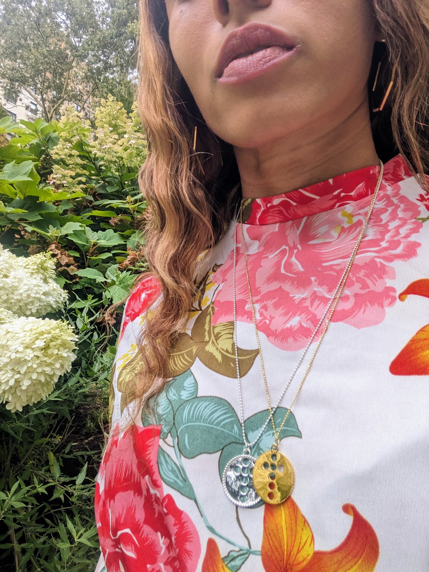 black woman in floral dress in garden wearing the cross cutout coin from the wandering jewel
