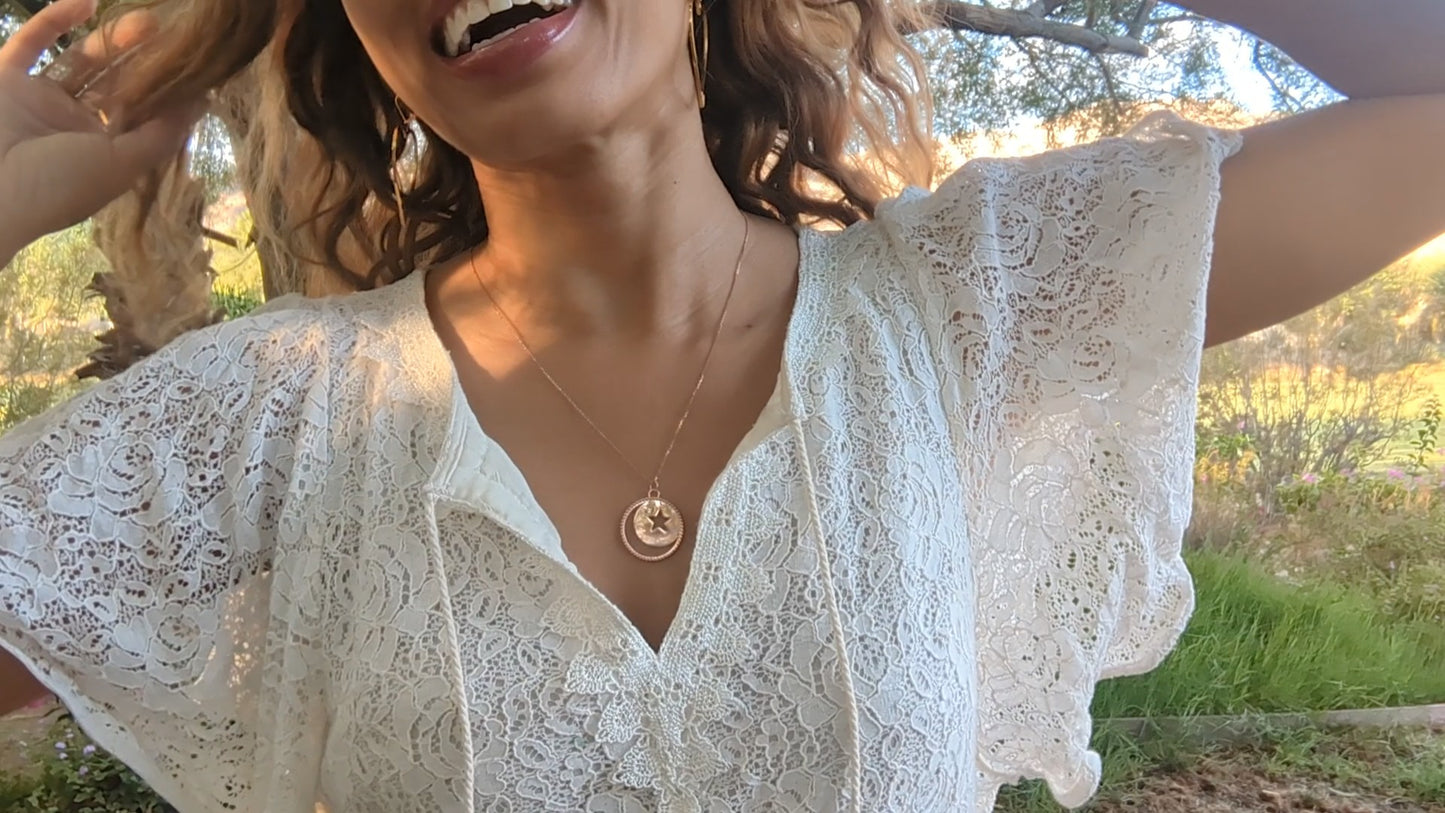 woman in white dress in a garden wearing the moon and Star cutout coin necklace from the wandering jewel