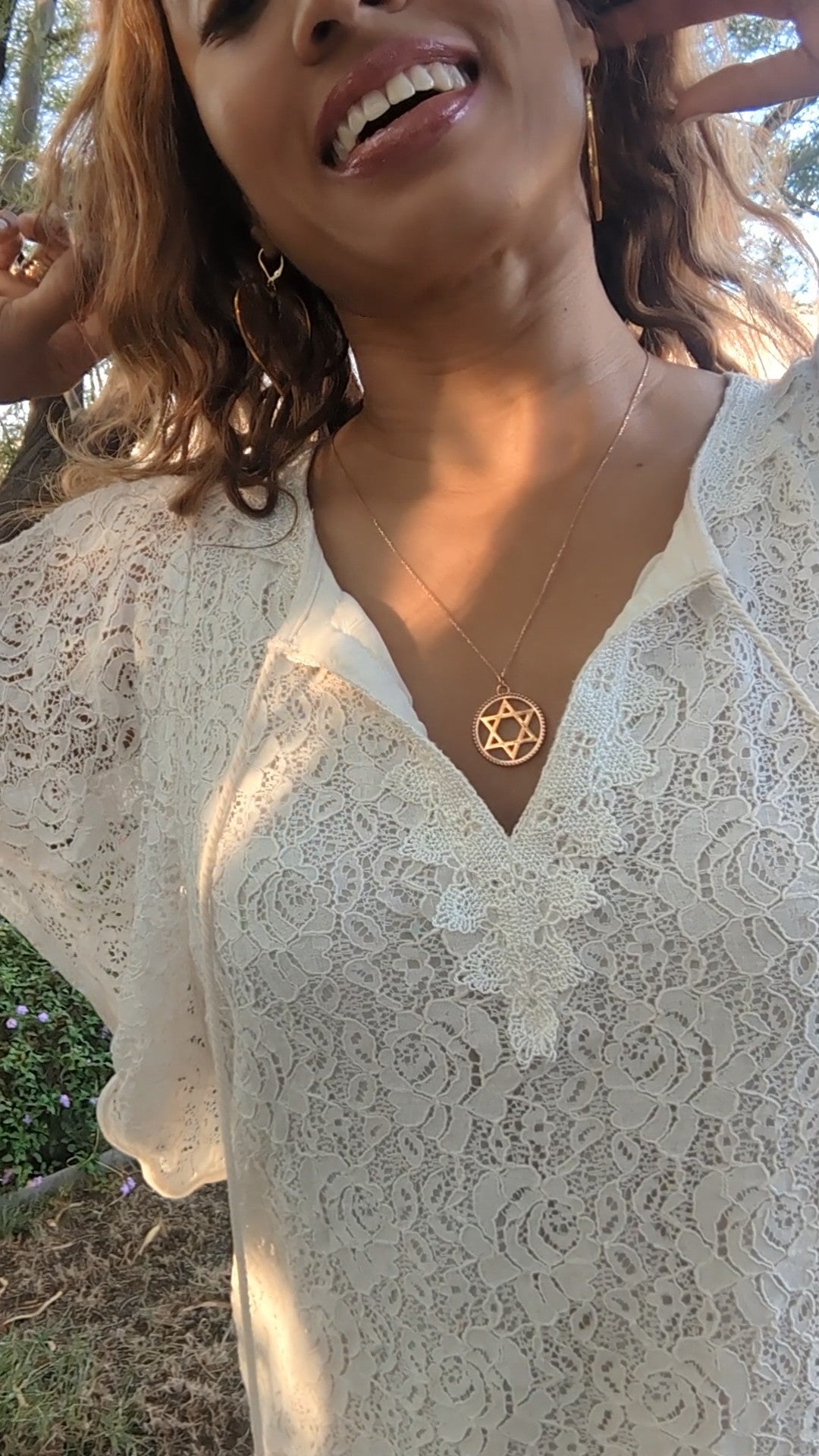 smiling black woman in white dress in a garden wearing the Rose gold star of David pendant necklace coin from the wandering jewel