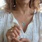 closeup picture of black woman in white dress in garden desert wearing the Jehovah cutout coin from the wandering jewel