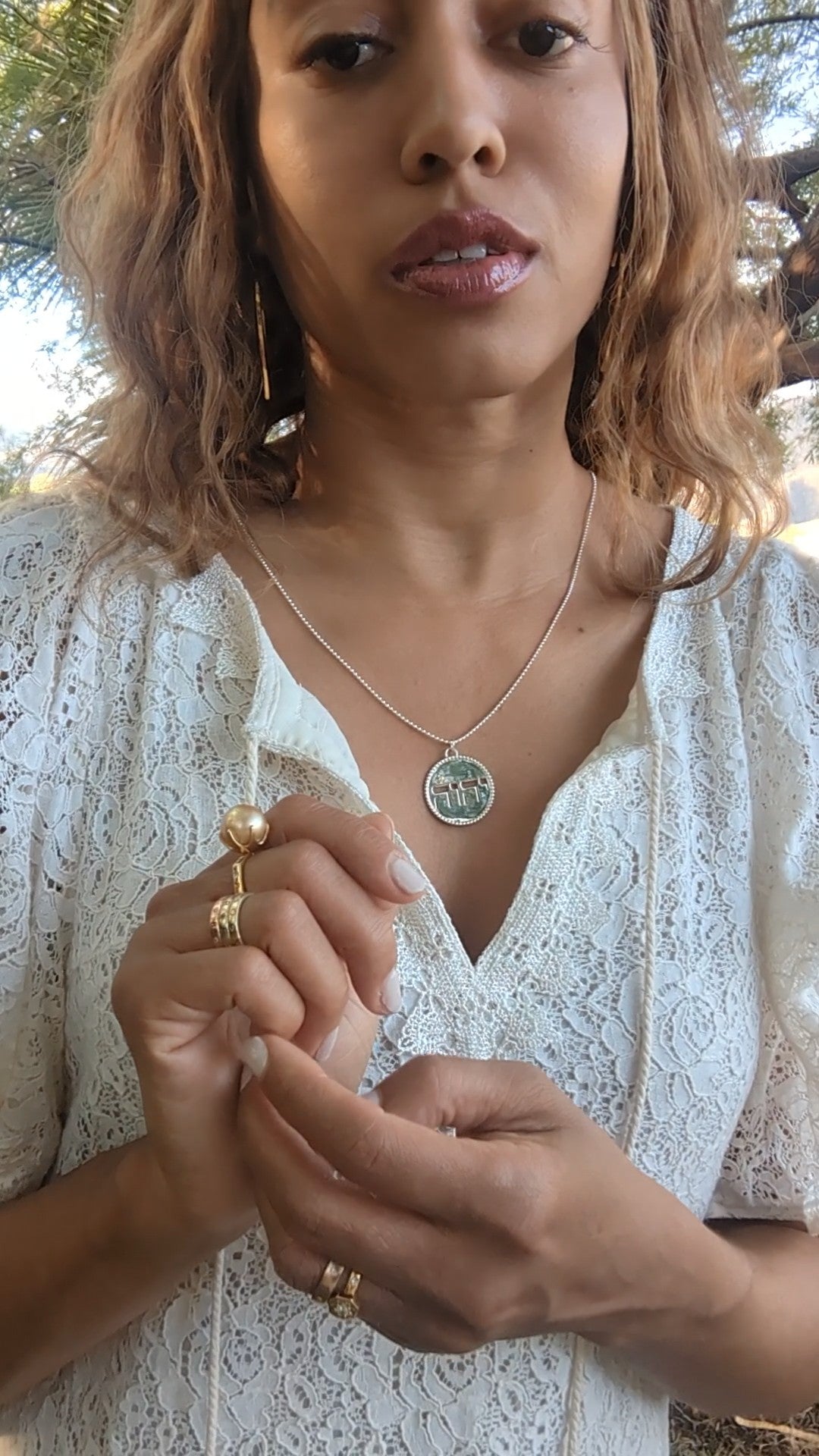 closeup picture of black woman in white dress in garden desert wearing the Jehovah cutout coin from the wandering jewel