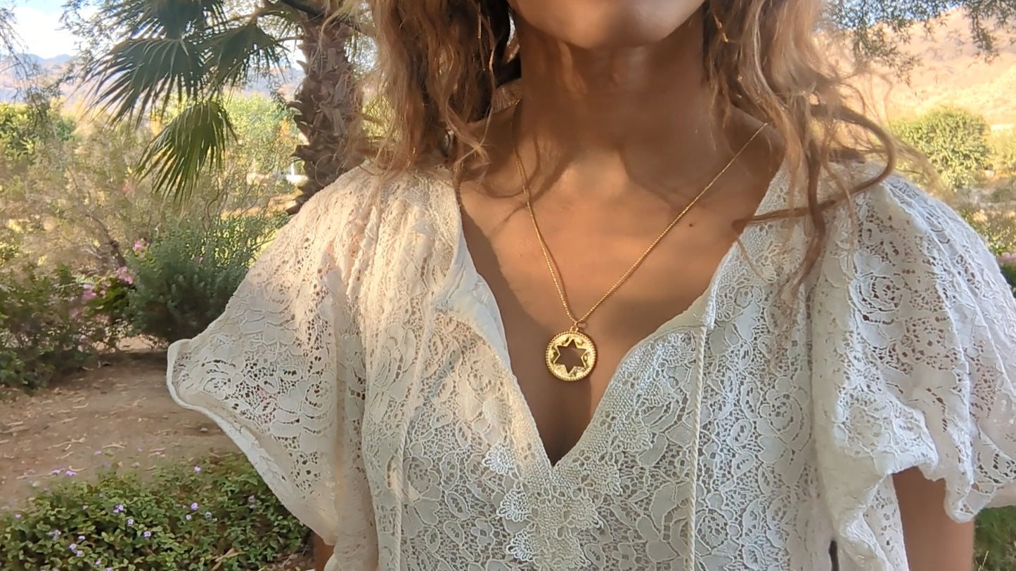 black woman in white dress in garden wearing the Rose gold star of David pendant necklace coin from the wandering jewel