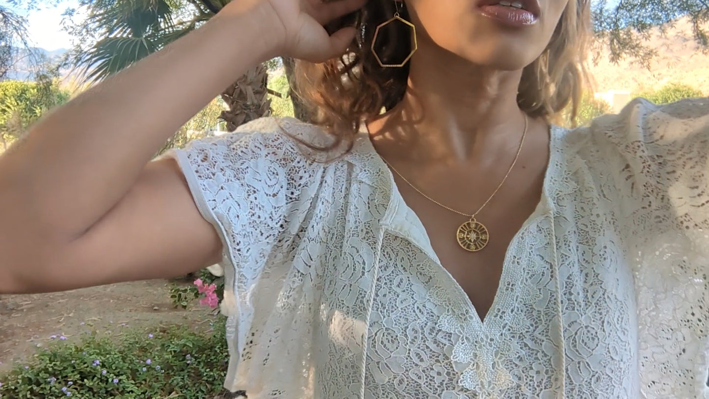 black woman in garden in a white dress wearing Large gold hoop diamond earrings septagon shaped from the wandering jewel
