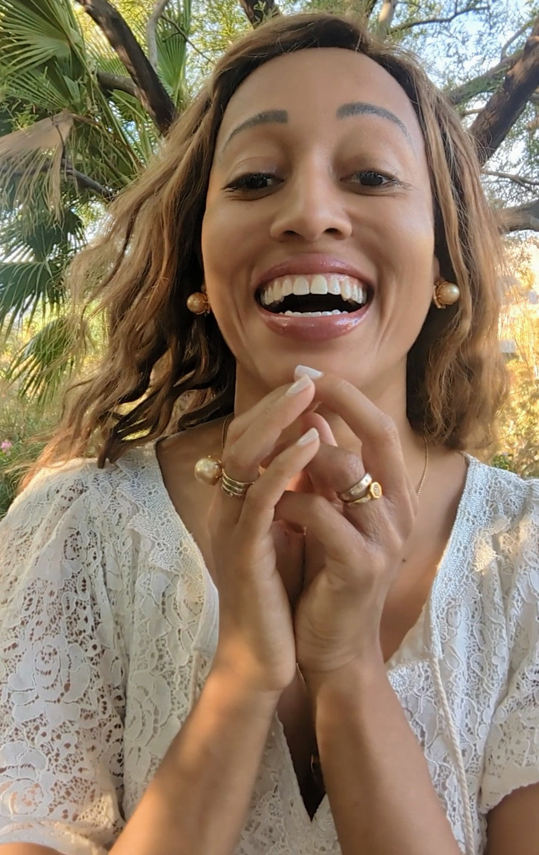 black woman with straight hair laughing  in garden in a white dress and wearing the gold septagon disengagement ring from the wandering jewel