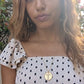 black woman in polka dot dress in Greek island wearing the cross cutout coin from the wandering jewel