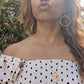 black woman in European village blowing air kisses in polka dot dress wearing Large gold hoop diamond earrings septagon shaped from the wandering jewel