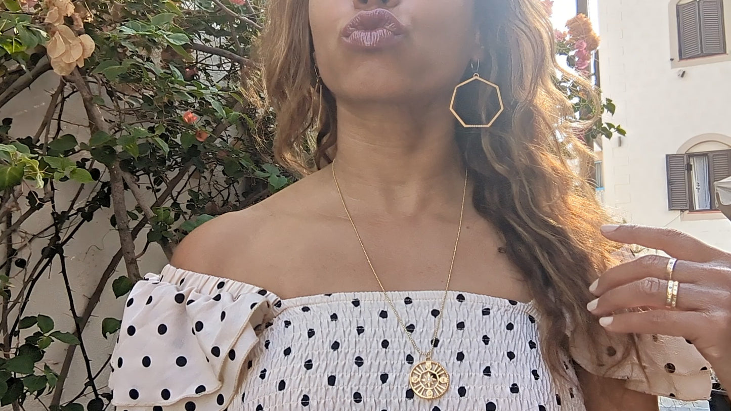 black woman in European village blowing air kisses in polka dot dress wearing Large gold hoop diamond earrings septagon shaped from the wandering jewel