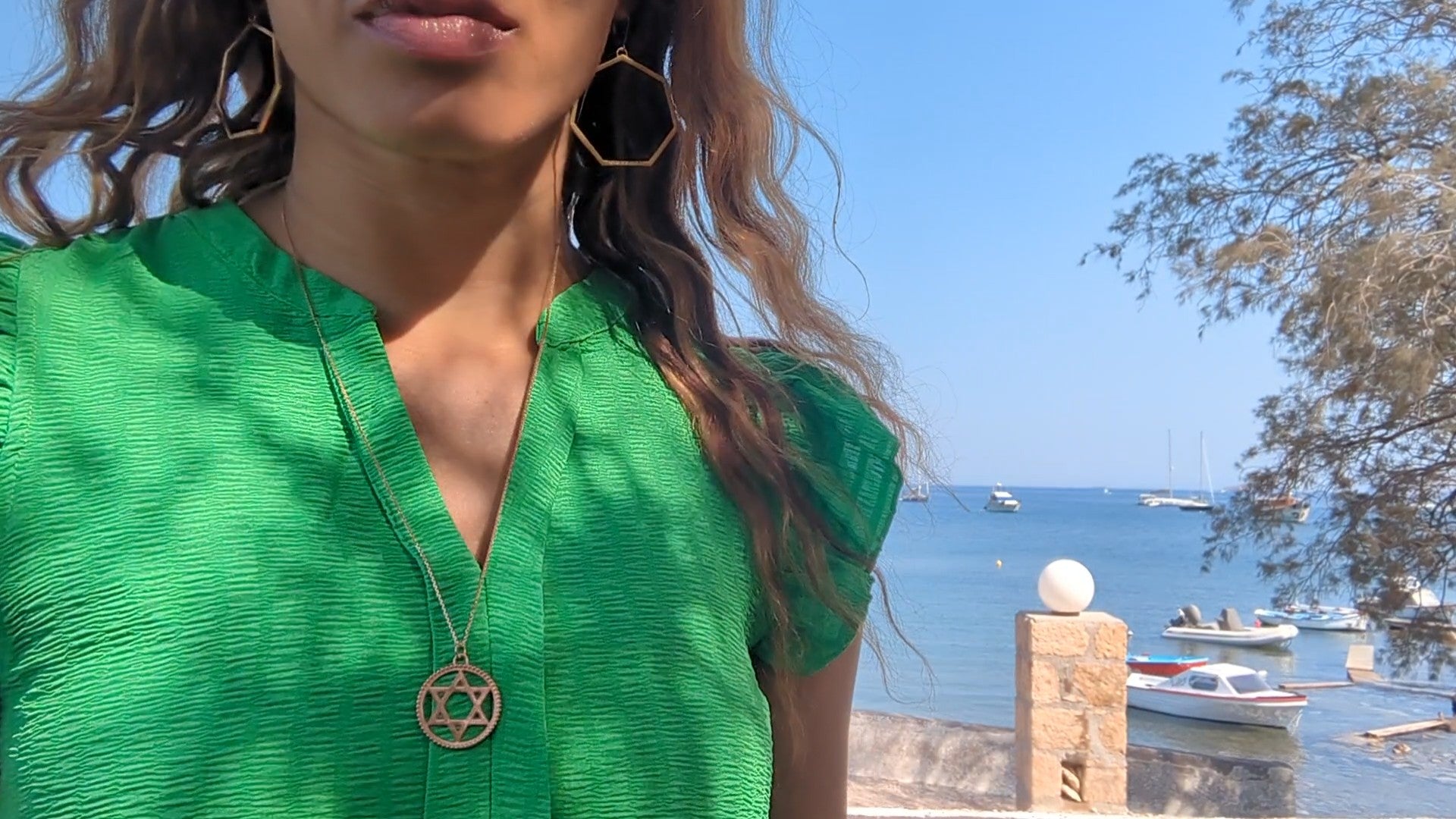 black woman on marina  in green dress wearing Large gold hoop diamond earrings septagon shaped from the wandering jewel