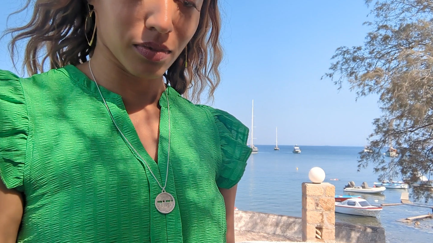 black woman in green dress in Greek harbor wearing the silver Jehovah pendant from the wandering jewel