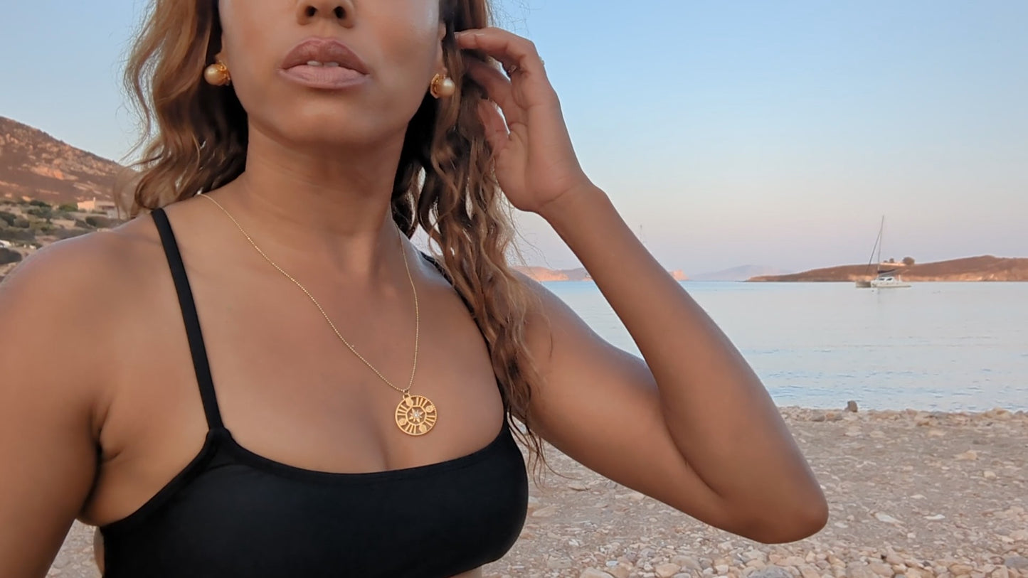  black woman on Greek beach in black bikini wearing large gold South sea pearl diamond earring studs from the wandering jewel