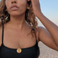 black woman in black bikini on Greek beach wearing the  Cross cutout coin from The Wandering Jewel