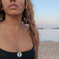 black woman in black bikini on Greek beach wearing  the cross cutout coin from the wandering jewel