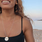 black woman on Greek beach in a black bikini wearing the Jehovah cutout coin from The Wandering Jewel