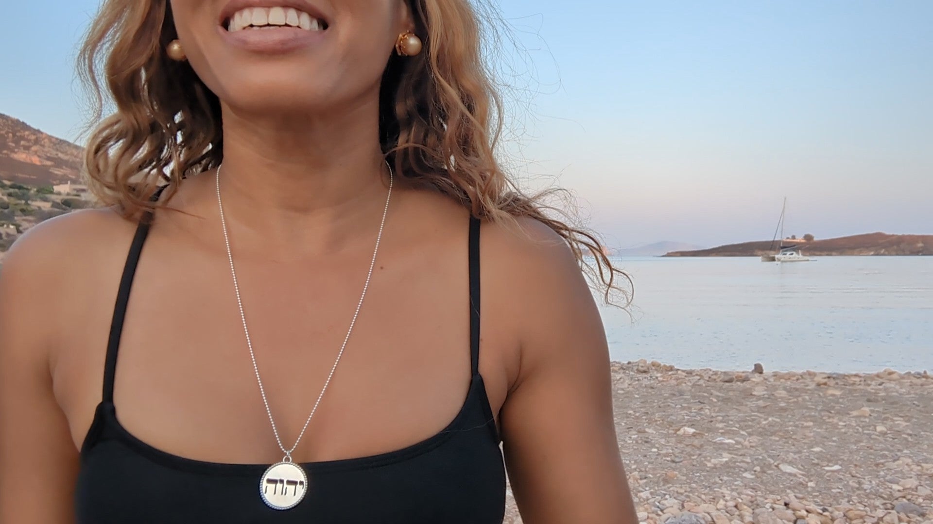 black woman on Greek beach in a black bikini wearing the Jehovah cutout coin from The Wandering Jewel