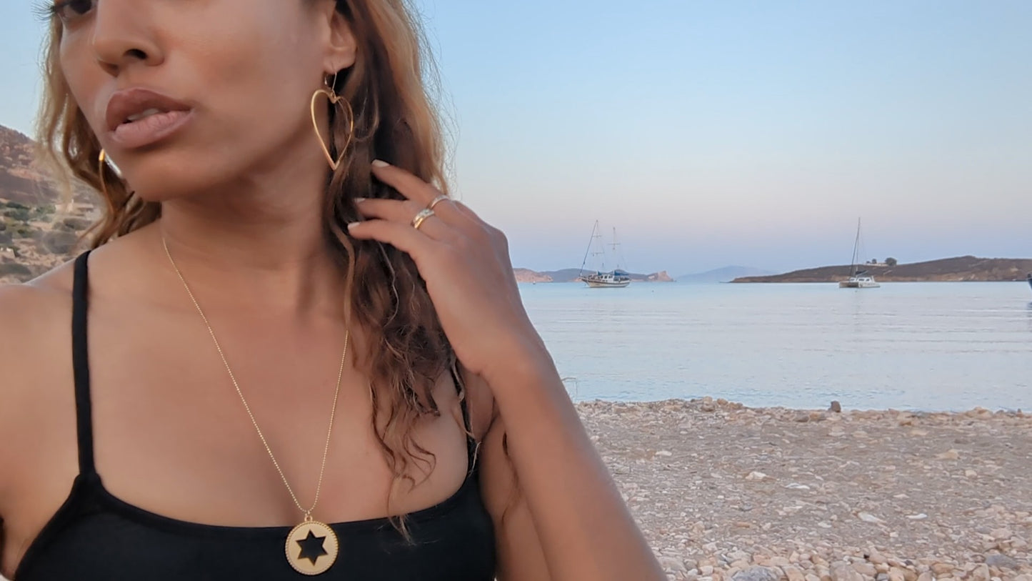 black woman on beach in black bikini wearing oversized hoop earrings shaped like a heart from the wandering jewel