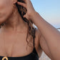 woman in black bikini on beach wearing large hoop earrings shaped like a heart form the wandering jewel