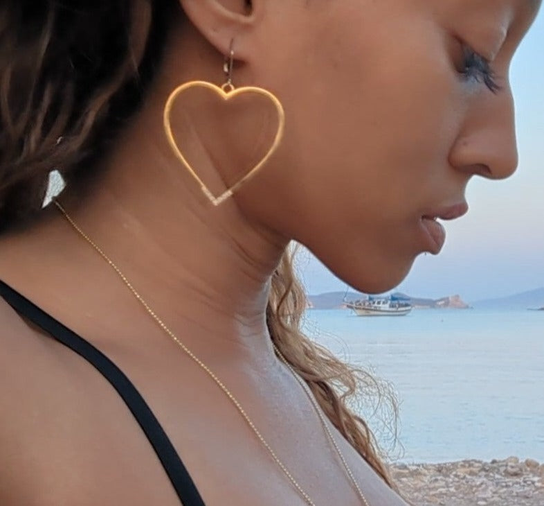 woman on beach in black bikini wearing a large hoop earrings shaped like a heart from the wandering jewel