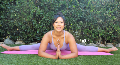 woman in leggings and tank top sitting in middle splits with hands in prayer position, she is wearing two 18K solid gold white jade pendants