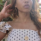 video of black woman in European village in polka dot dress wearing Large gold hoop diamond earrings septagon shaped from the wandering jewel