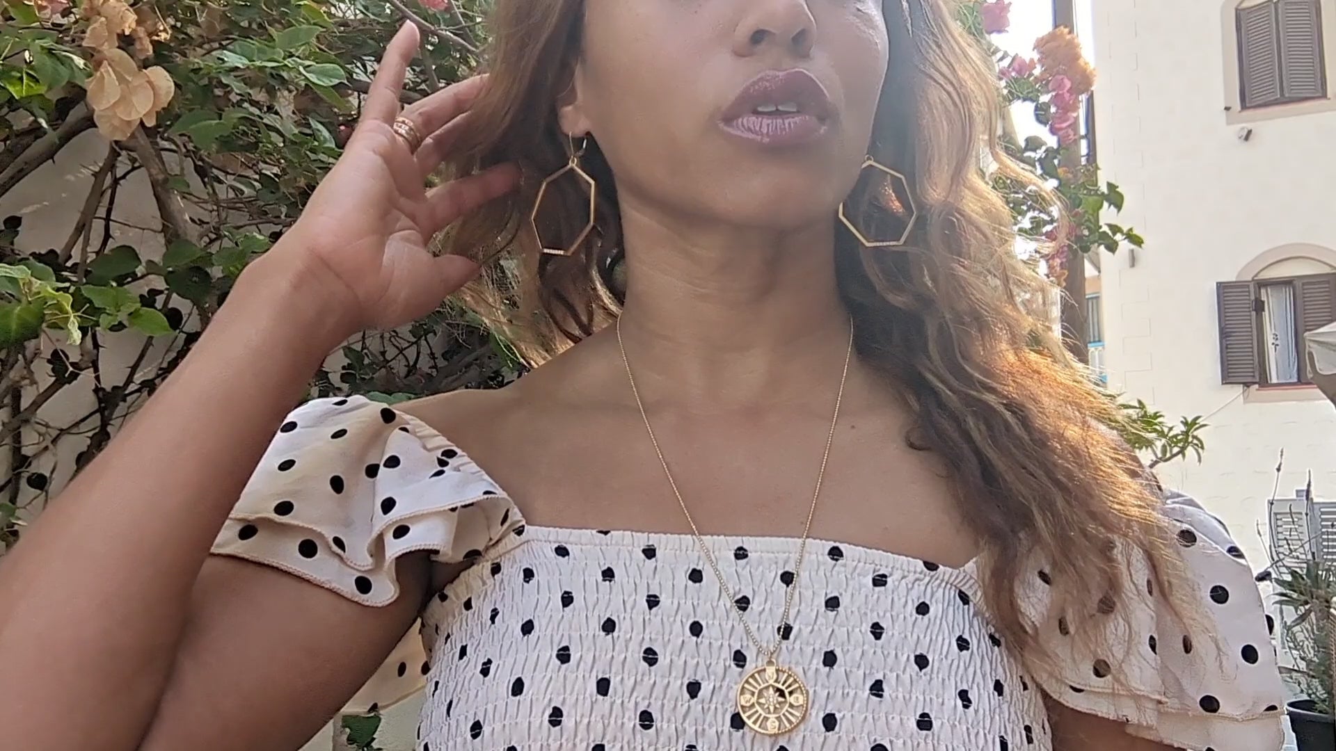 video of black woman in European village in polka dot dress wearing Large gold hoop diamond earrings septagon shaped from the wandering jewel