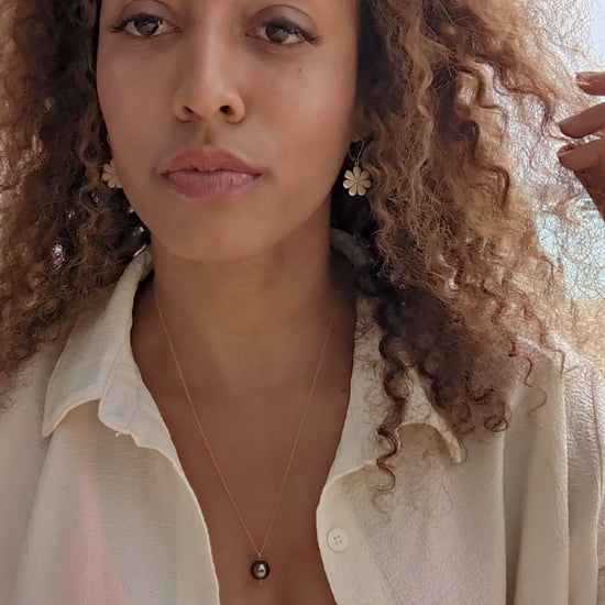 video of black woman with curly hair on beach in bikini with oversized white blouse wearing the black South sea pearl pendant from the wandering jewel