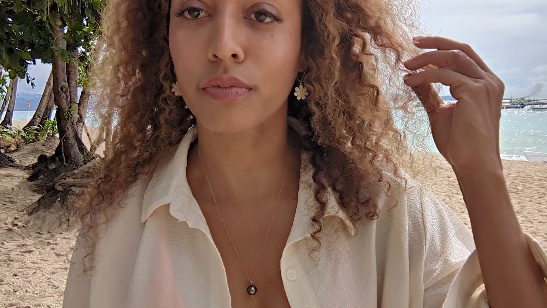 video of black woman with curly hair on beach in bikini with oversized white blouse wearing the black South sea pearl pendant from the wandering jewel
