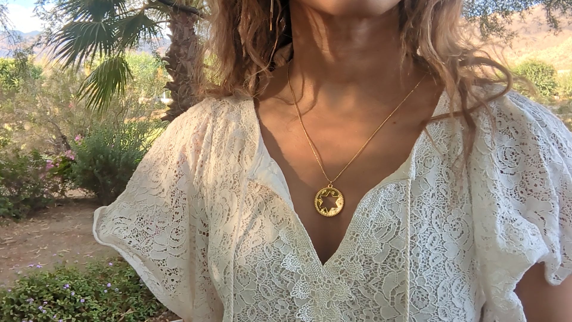 black woman in white dress in a garden wearing Rose gold star of David pendant necklace coin from the wandering jewel