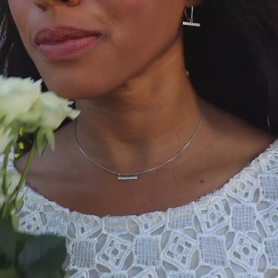 video of woman white dress in front of a picket fence wearing the 7 diamond horizon earrings from the wandering jewel