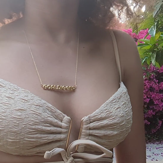 woman in tan bikini top wearing  the gold goal digger necklace from the wandering jewel