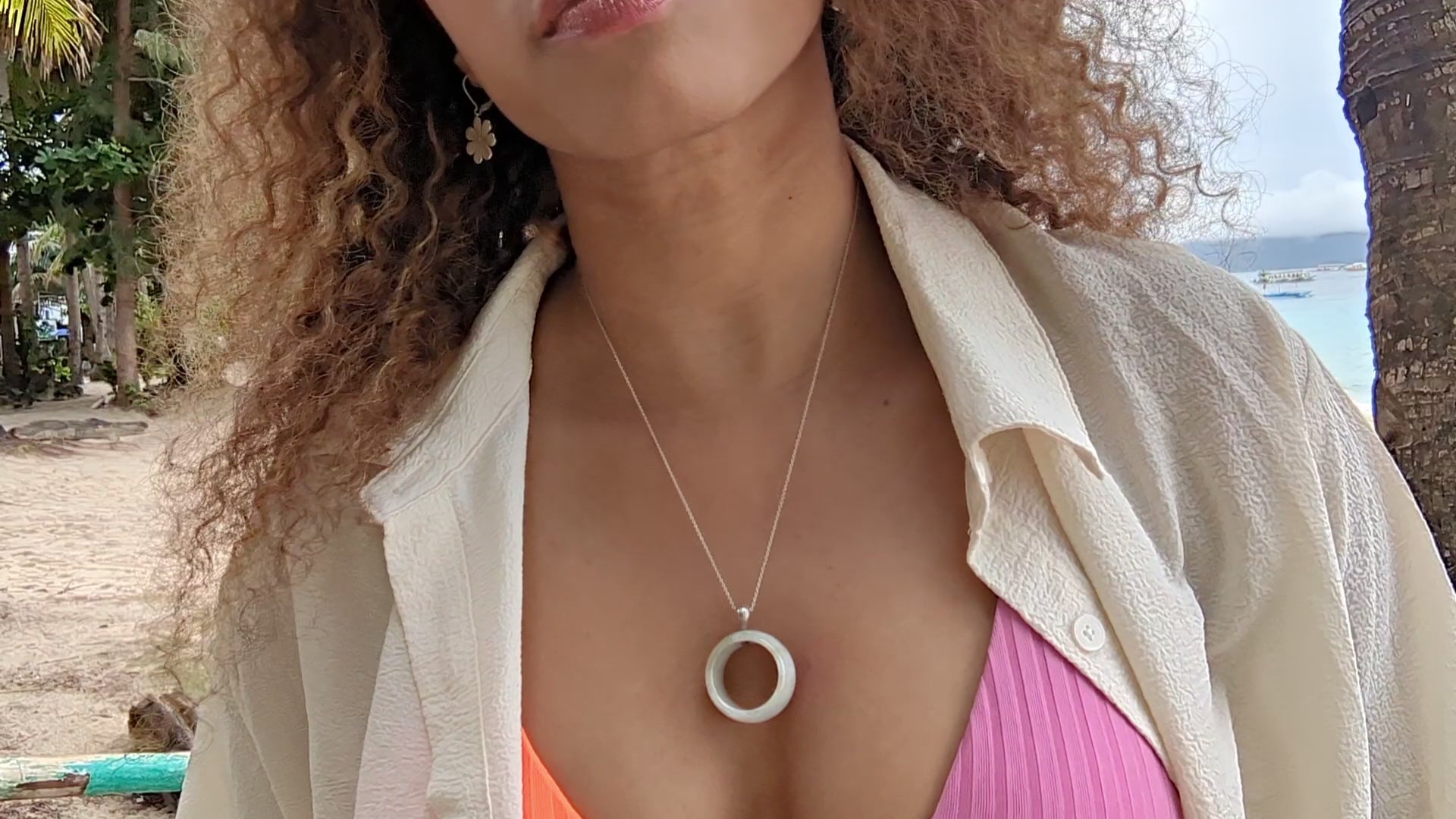 video of woman at beach in a white blouse and pink and orange bikini wearing a white jade necklace from the wandering jewel