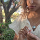 video of woman in white dress in garden wearing the silver cross cutout coin from the wandering jewel