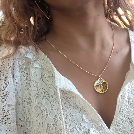 video of black woman in white dress in garden desert wearing the Jehovah cutout coin from the wandering jewel