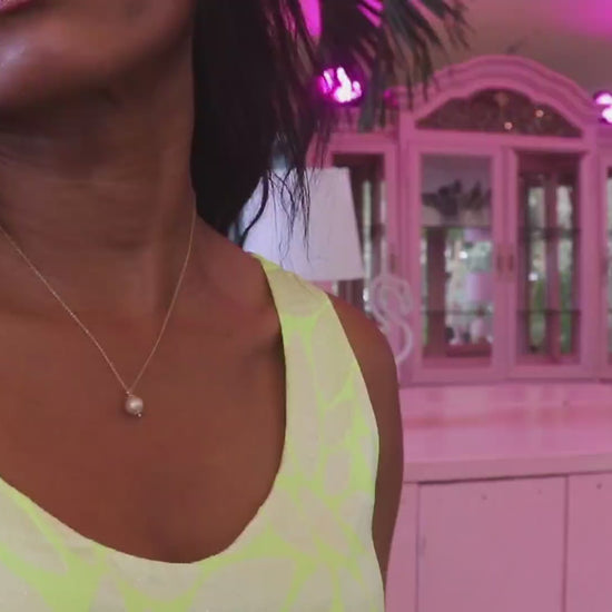 video of black woman with straight brown hair in a neon yellow dress standing in front of a pink room  and wearing a the queen bee golden South sea pearl necklace from the wandering jewel
